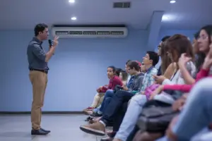 Palestrante conduz reunião estratégica com equipe sentada, discutindo estrutura comercial e liderança empresarial em ambiente corporativo.