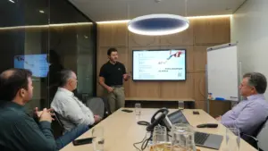 Consultor apresenta estratégia de metas e gestão comercial para equipe em reunião corporativa, com dados projetados em tela e apoio de quadro branco.